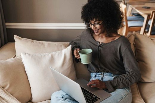 A person sits on a couch with a laptop and a mug.