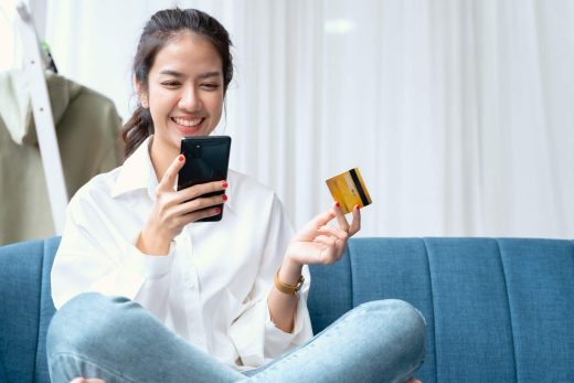 A person smiles while holding a smartphone and a credit card, seemingly engaged in online shopping.