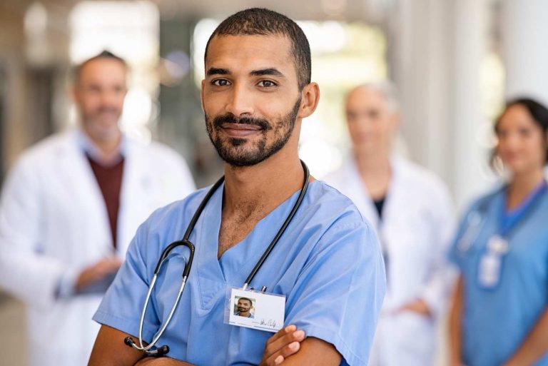young male doctor smiling while standing in hospital corridor with healthcare team in background