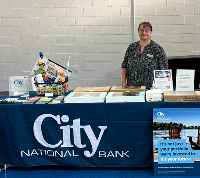 A person stands behind a table with a City National Bank banner and promotional items