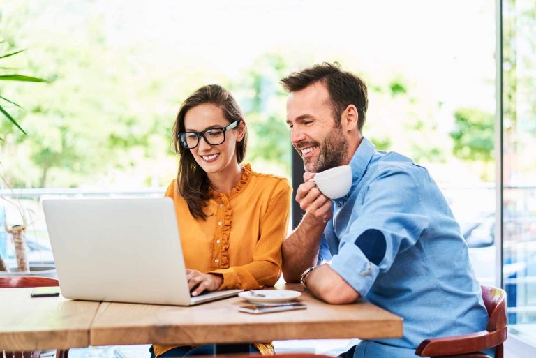 A man and woman sitting at a cafe table looking at a laptop