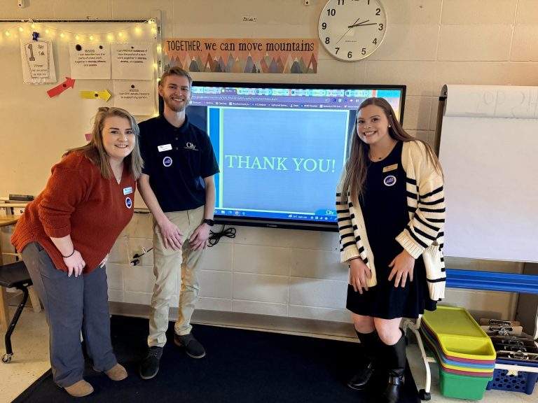 3 people stand in front of a large screen displaying "THANK YOU!"