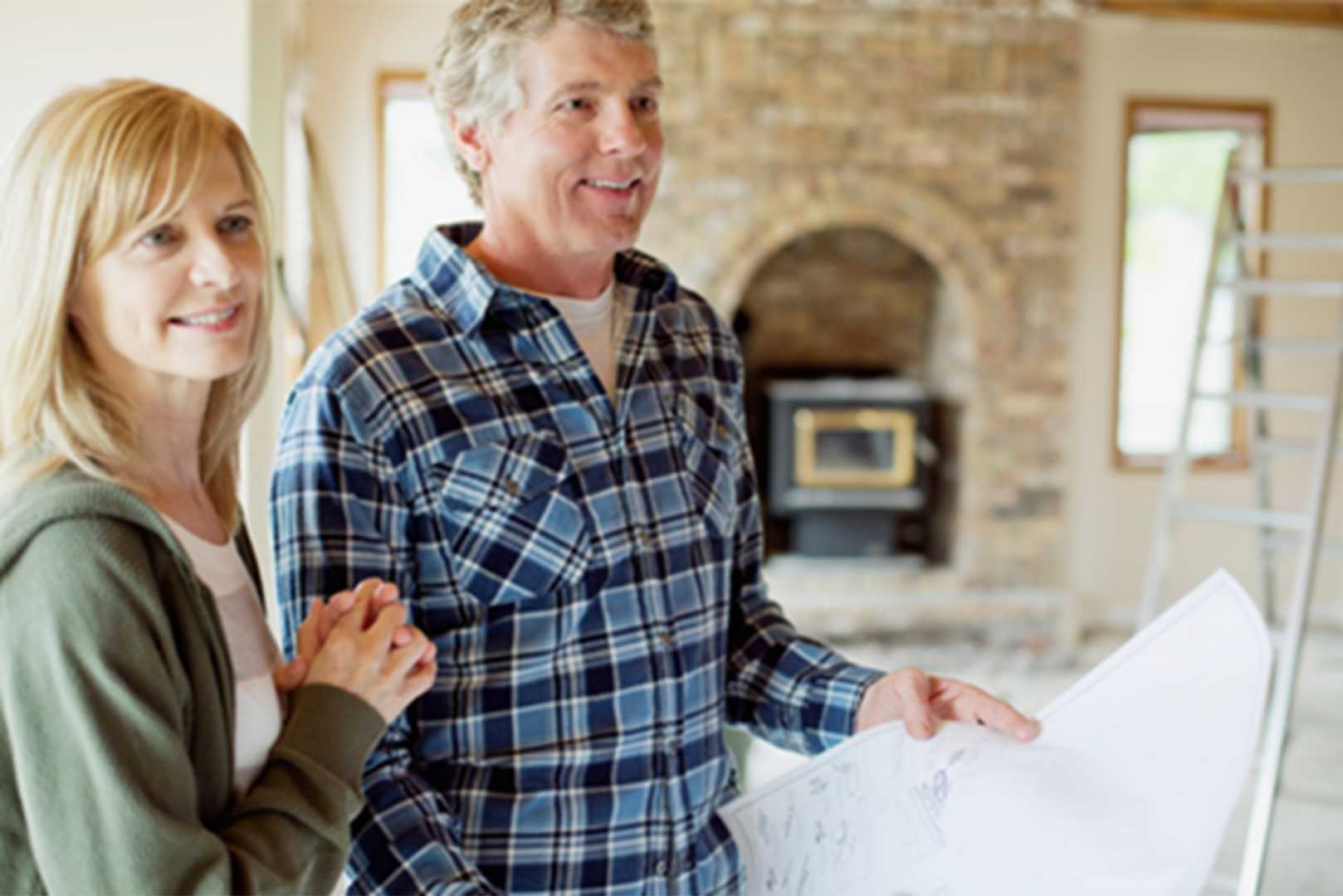 A man holding blueprints while standing next to a woman, in a room that is under renovation