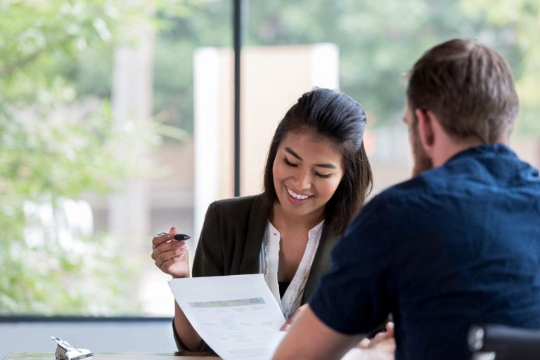 young female bank loan officer smiles as she reviews a loan application with a male customer