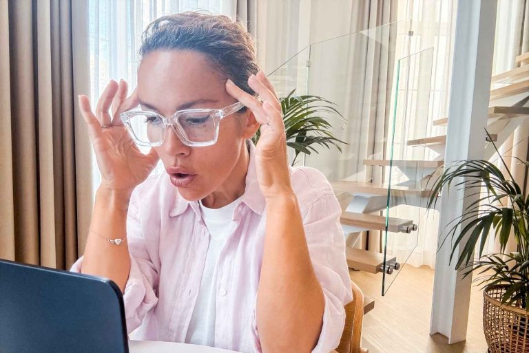 A woman is looking at a laptop with their hands on their temples, appearing stressed.