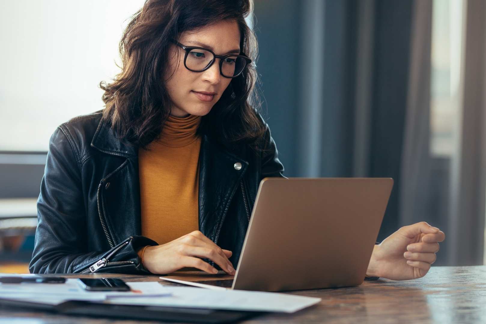 A woman is typing on a laptop at a table with papers.