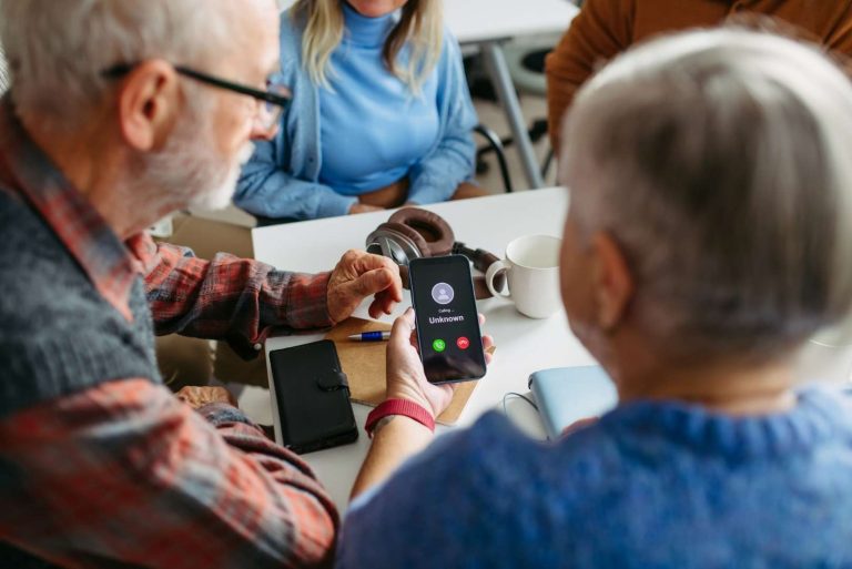 An older person holds a smartphone displaying an incoming call from an unknown number