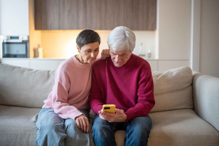 An older couple looking at a yellow smartphone together while sitting on a sofa.