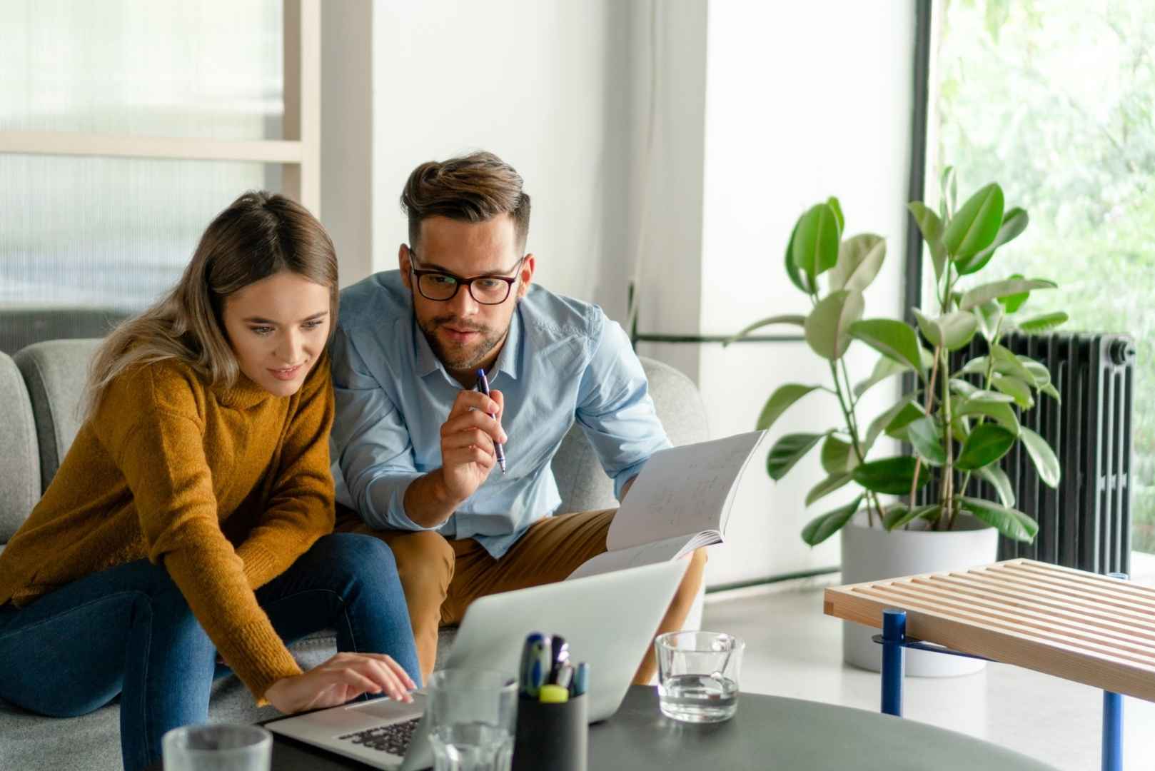 A man and a woman sitting on a couch, looking at a laptop.