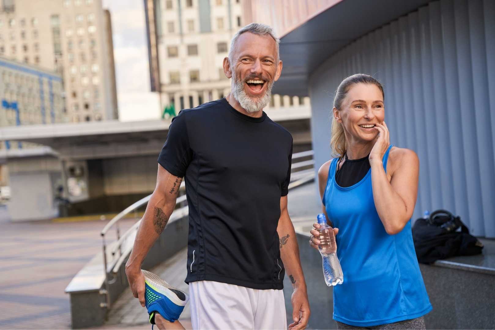 A man stretches his leg while a woman stands beside him holding a water bottle.