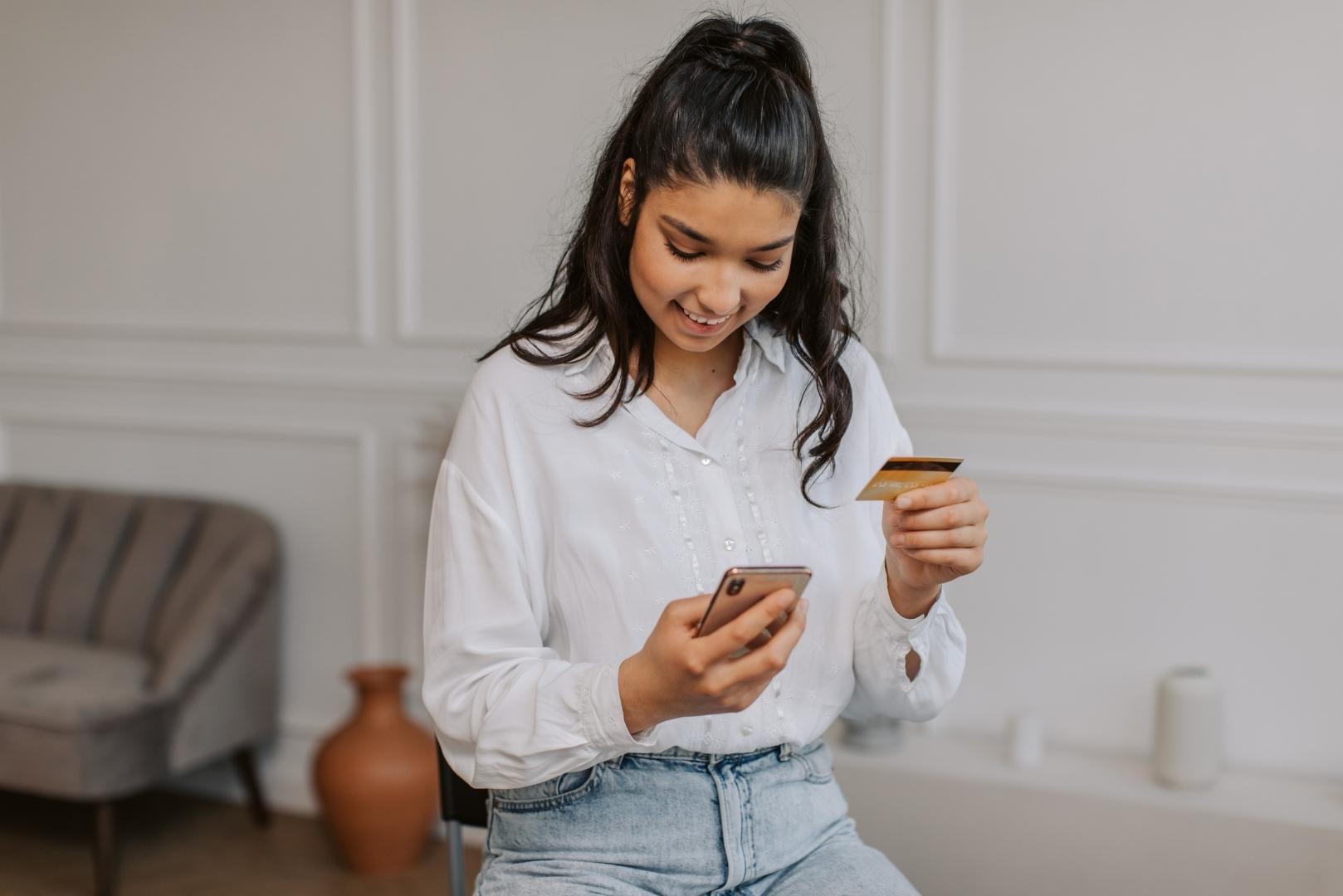 A woman holding a smartphone and a credit card, appearing to make an online purchase.