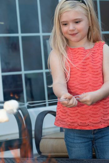Little girl roasts marshmallows over a fire pit.